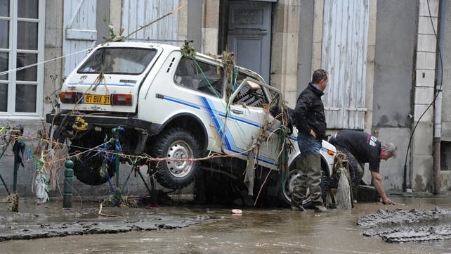 Inhabitants stand next to a damaged car on a mud covered street in Saint-Beat