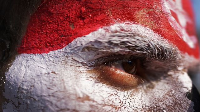 A man with his face painted the colors of the Egyptian flag looks out as thousands of protesters celebrate