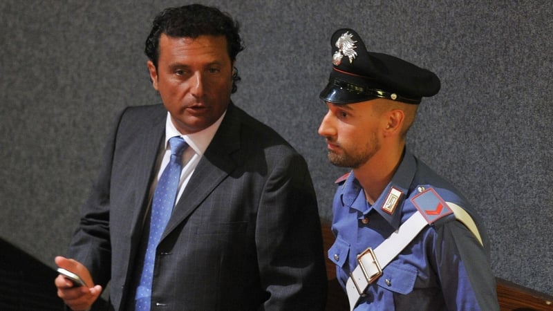 Francesco Schettino speaks to a policeman as he takes his place for his trial in Grosseto