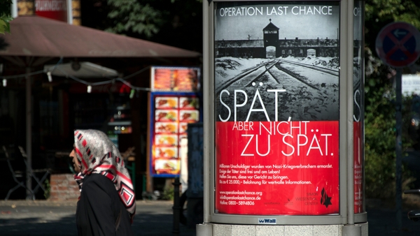 The poster features the infamous gates of Auschwitz along with the slogan 'Late, but not too late'
