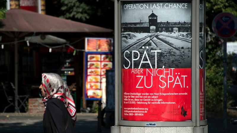 The poster features the infamous gates of Auschwitz along with the slogan 'Late, but not too late'
