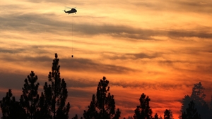 A helicopter prepares to drop water on the fire