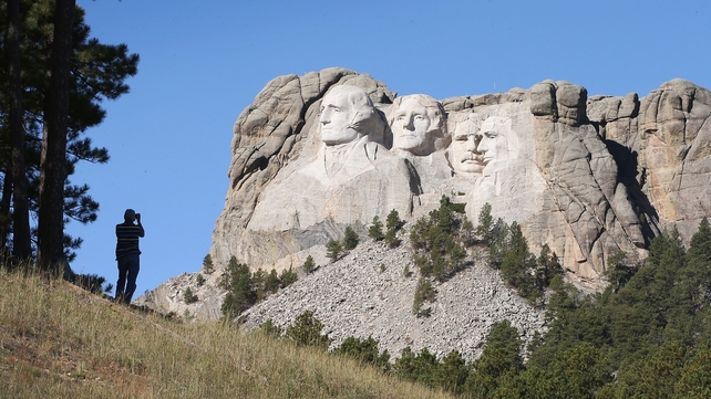 A tourist takes a picture of Mount Rushmore from a nearby field
