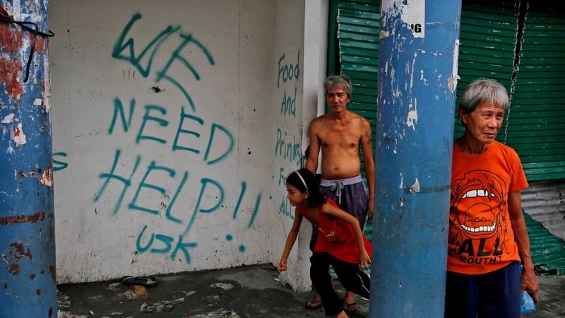 People stand next to grafitti requesting aid in Tacloban