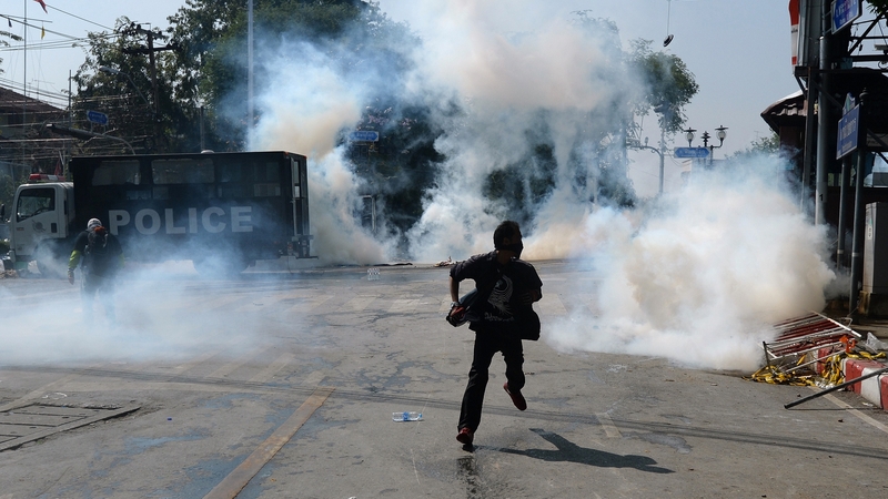 An anti-government protester runs as police fire tear gas shells at them outside Government house