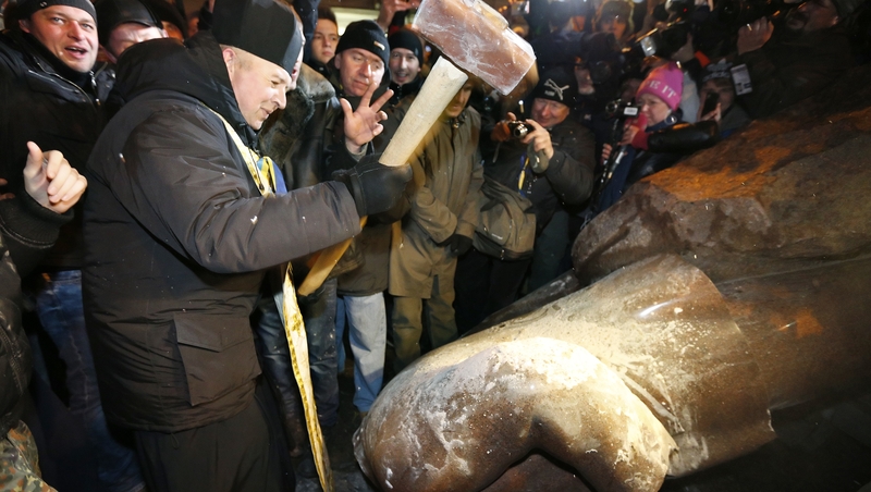A priest hammers at a statue of former Soviet leader Vladimir Lenin as others gather around after it was toppled during a protest