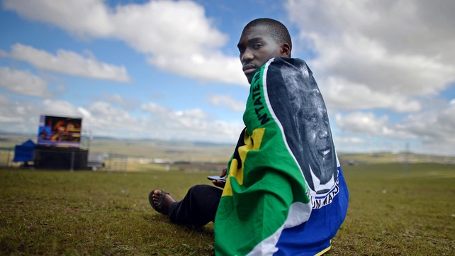 A supporter draped in a flag bearing Nelson Mandela's image watches proceedings on a screen