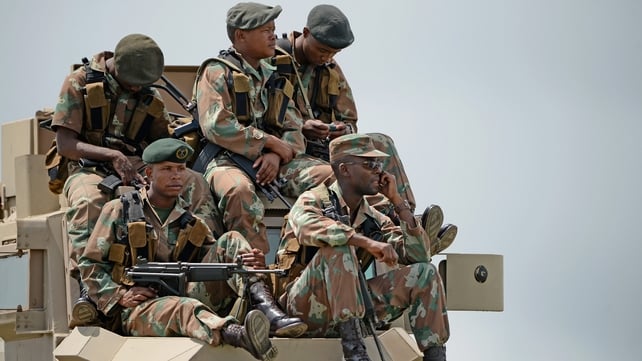 Soldiers watch the ceremony on a large screen while keeping watch on the gathering crowds