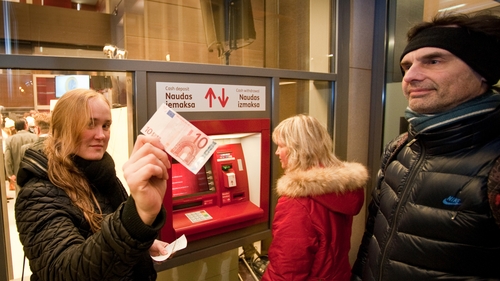 A woman shows a €10 note after withdrawing it from a cash machine in Riga