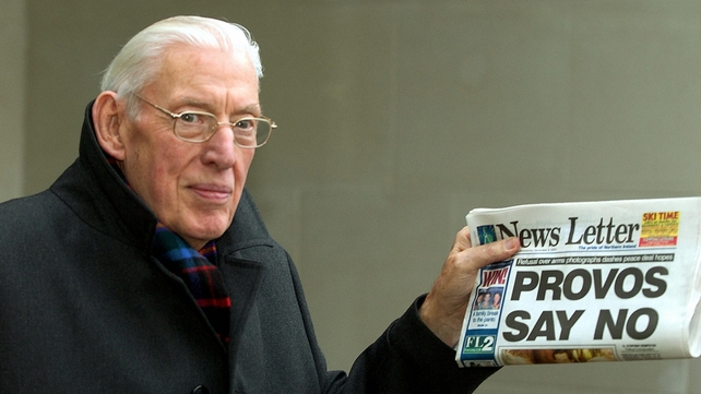 Mr Paisley smiles as he holds up a newspaper on 8 December 2004. His party refused to share power with Sinn Féin if there was no photographic proof the IRA had surrendered its complete arsenal