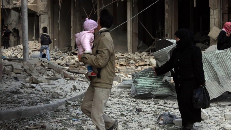 Syrians walk along a destroyed street following a reported airstrike by government forces on the northern Syrian city of Aleppo