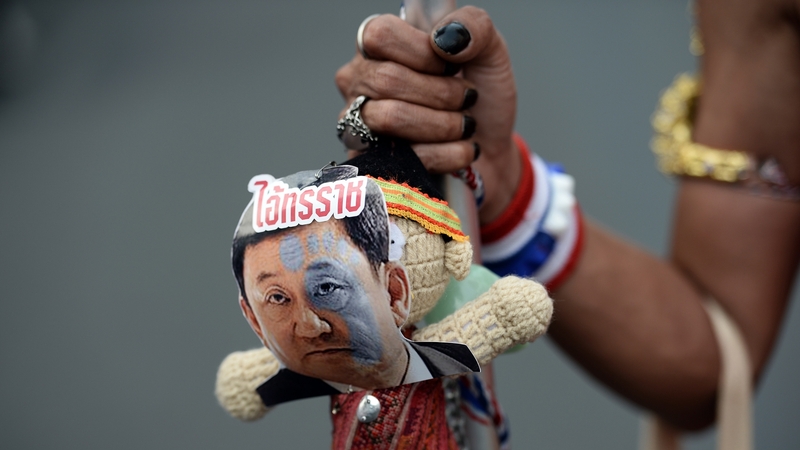 An protester holds a doll with a picture of former PM Thaksin Shinawatra and the word 'tyrant'