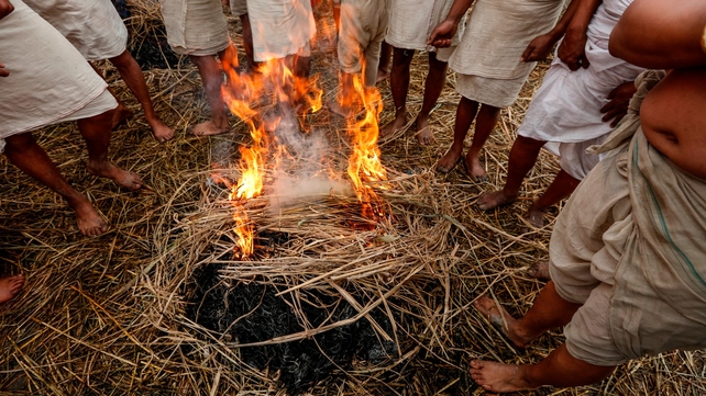 Devotees warm up by a fire before taking their holy bath (Pic: EPA)