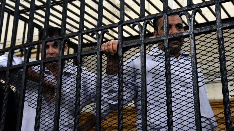 Two policemen Mahmoud Salah (L) and Awad Ismael (R) stand inside a court cage during their trial