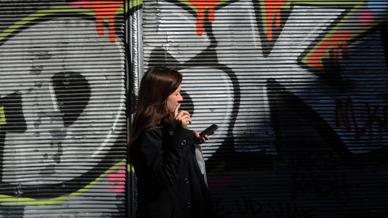 A Turkish woman uses her smartphone as she stands by a graffiti wall, on Istiklal street, in Istanbul