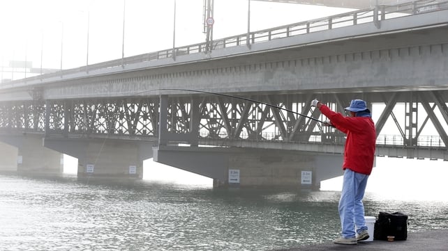 A fisherman tries to catch fish as the Auckland Harbour Bridge is covered in a blanket of fog in New Zealand