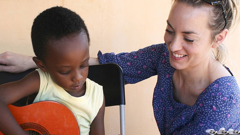 Kathryn Thomas looks on as a young Rwandan learns their guitar chords