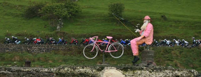 The Peloton travels along the North Antrim Coast on Saturday, watched by a giant cyclist who is doing some fishing