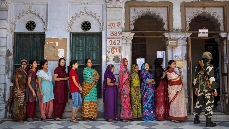 A border police officer stands guard as Indians wait in line to vote at a polling station in Varanasi