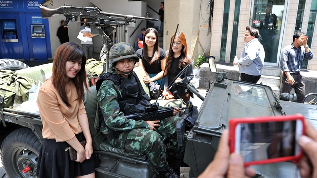 Passers by pose for a photo with Thai army soldiers standing guard on a city centre street