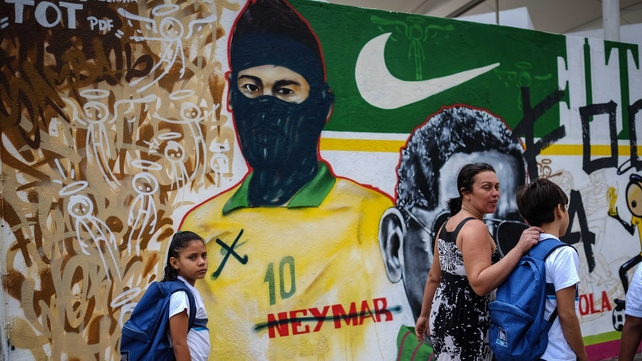 People walk past graffiti depicting Brazilian national footballer Neymar with a hood used by members of the anarchist group known as Black Bloc