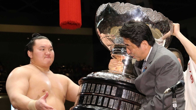 Japanese Prime Minister Shinzo Abe (C) is helped to carry the Prime Minister's Cup as he gives it to Yokozuna Hakuho (L) after the Summer Grand Sumo tournament in Tokyo