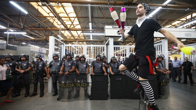 A juggler on a unicycle performs in front of police during an anti-World Cup protest at the Carrao Metro Station