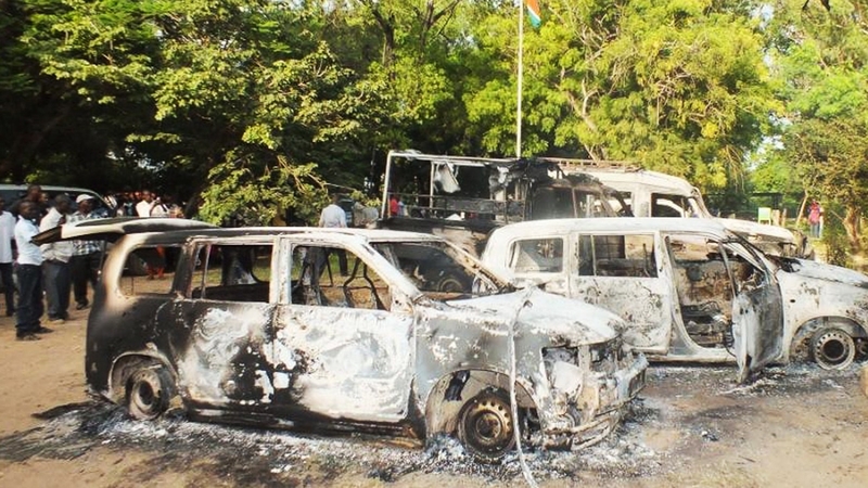 People gather next to charred vehicles outside a police station in Mpeketoni after the attacks