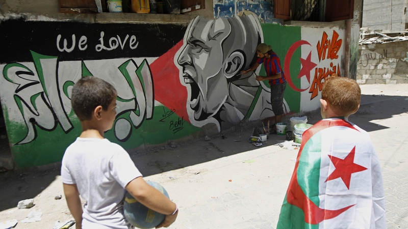 Palestinian boys, one weraing an Algerian flag, looks at graffiti-artist, Belal Khaled painting a portrait Italian football player Andrea Pirlo in Gaza