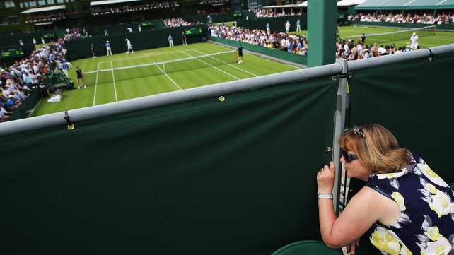 A fan peaks through a gap in the fence to watch the action at Wimbledon