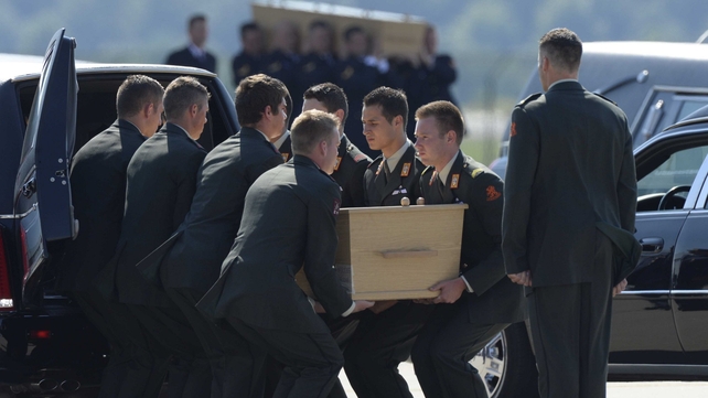 One of the coffins is placed into a hearse at the airport