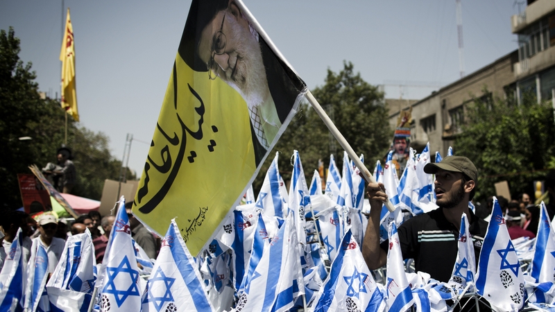 A man waves a picture of Ayatollah Ali Khamenei above Israeli flags before setting the flags on fire during a demonstration in Tehran