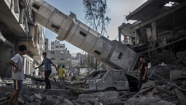Palestinians walk next to the collapsed minaret of a destroyed mosque in Gaza City