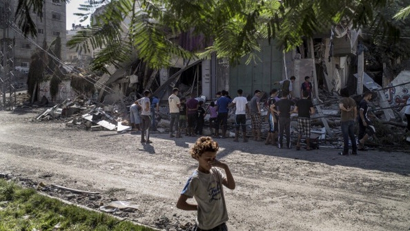 A Palestinian child covers her eyes to protect them from dust flying from a house hit by an Israeli military strike