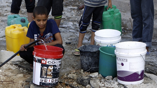 A Palestinian man and children fill containers with water from a broken main in Gaza City's al-Shejaea neighbourhood