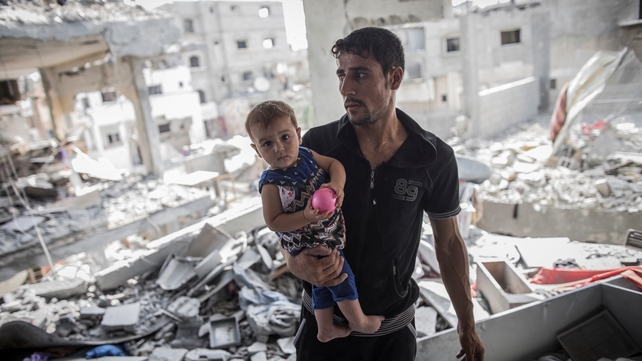 A Palestinian man holds his baby in the ruins of their destroyed home in Beit Hanoun