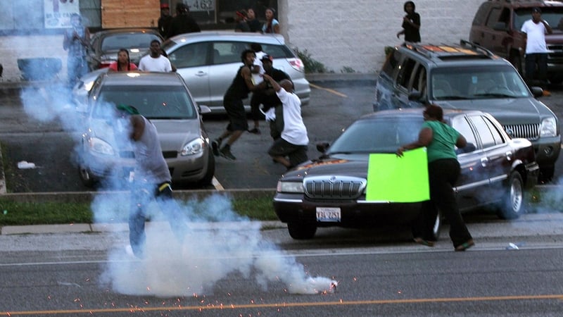 People scatter as St Louis County Tactical Police officers fire tear gas along West Florissant Road