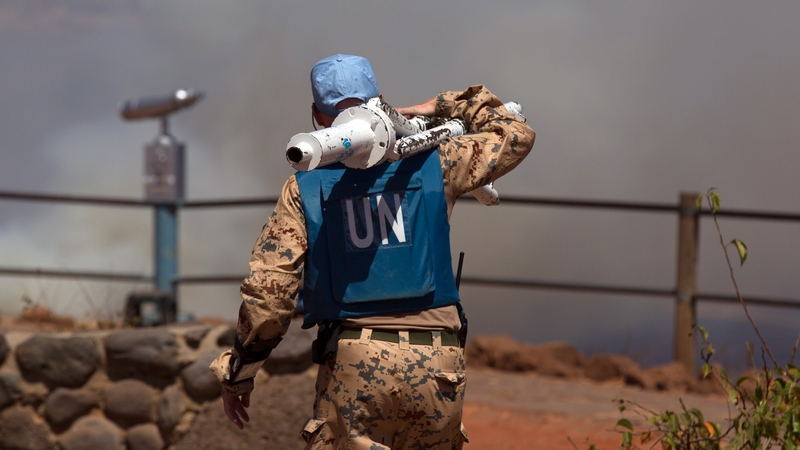 A UN peacekeeper carrying equipment as smoke rises in the background at the Syrian-Israeli border