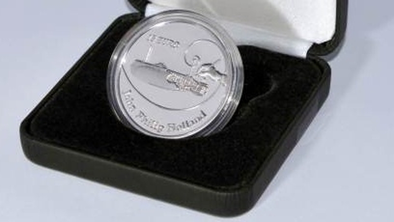 The coin features an image of the inventor’s hand poised to place the final stroke of a technical drawing