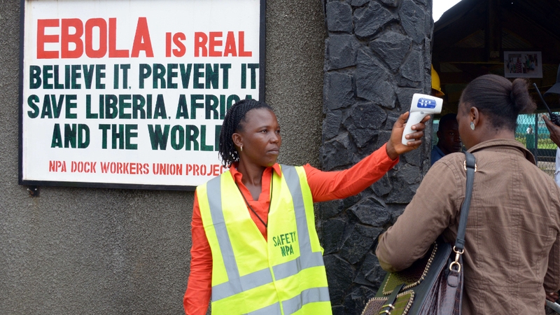 A security agent controls the temperature of a woman at the entrance of the port of Monrovia, Liberia
