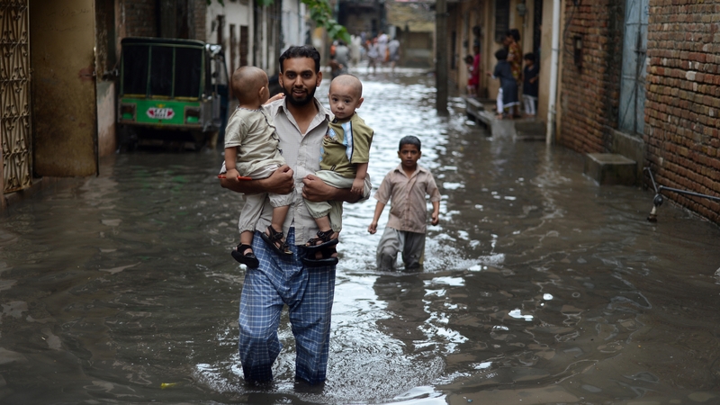 A man carries young children along a flooded street after the heavy rain in Rawalpindi