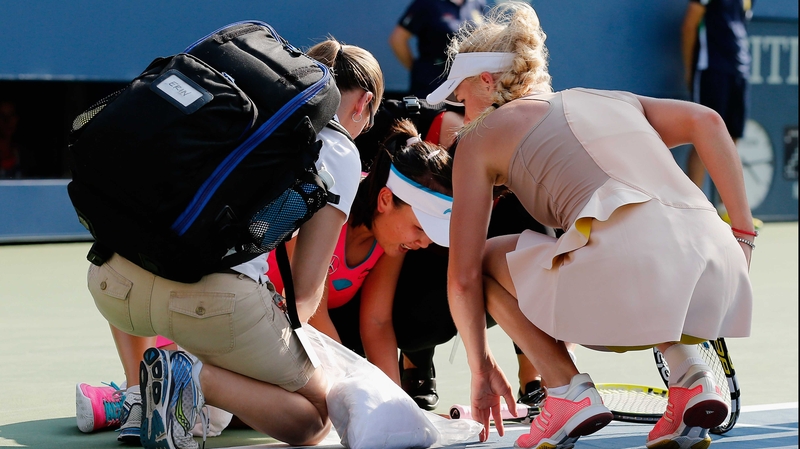 Caroline Wozniacki (R) of Denmark looks on as Shuai Peng (C) of China is tended to by trainers