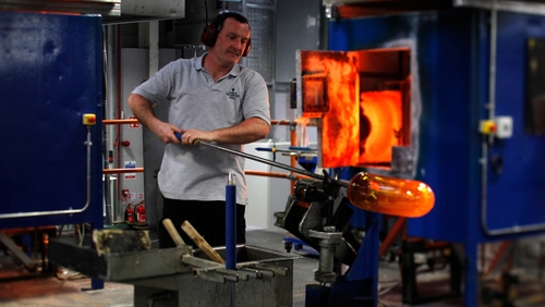 A craftsman shapes a bowl by blowing air into it, after heating the glass in the furnace, at the Waterford plant in 2010