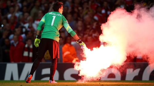 Galatasaray goalkeeper Fernando Muslera carries a flare off the pitch at the Emirates