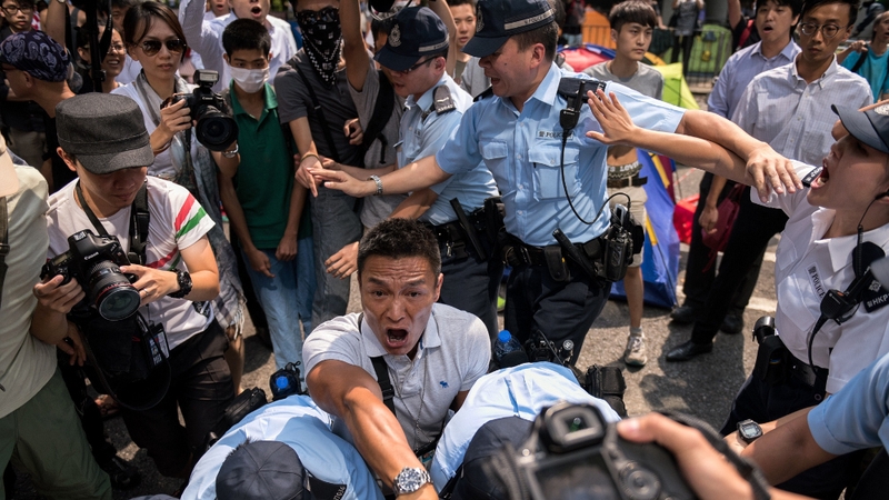 A police officer (C) shouts at people to move back after detaining a man who had attacked pro-democracy protesters