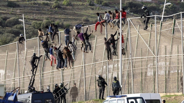 Migrants try to climb up a border fence in a mass attempt to jump into Melilla, the Spanish exclave in northern Africa
