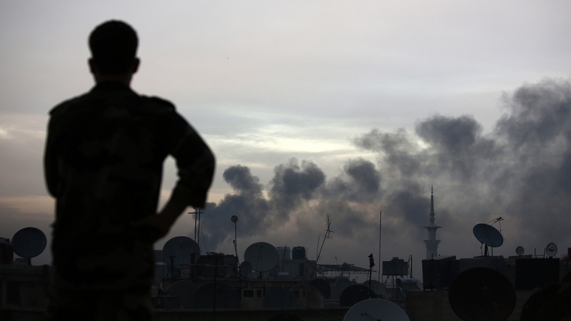 A man watches smoke rise from the Tall Kurdi region as he stands on the roof of his house in Douma