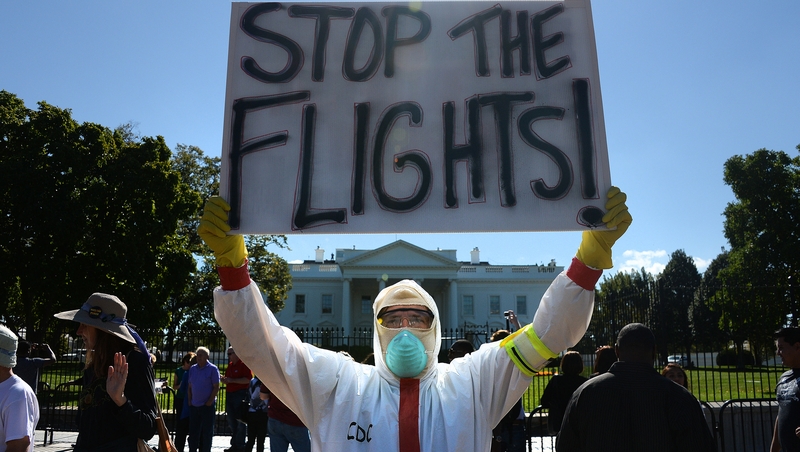 A protester stands outside the White House with a placard asking President Obama to ban flights in effort to stop Ebola