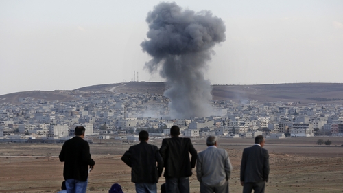 Local residents watch smoke from an explosion rising over the Syrian city of Kobane