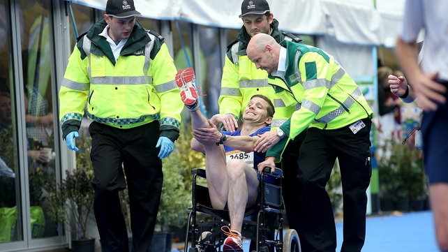 A runner with cramp is helped over the line